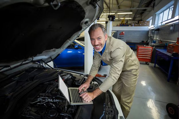 mechanic using a laptop with a car